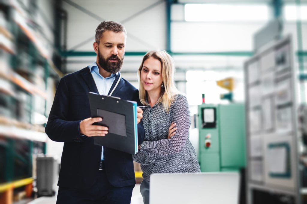 A portrait of an industrial man and woman engineer with laptop in a factory, working.